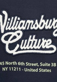 Tessuto blu navy con testo ricamato bianco che recita "Cultura di Williamsburg." Testo dell'indirizzo verde sottostante: "45 North 6th Street, Suite 3B, NY 11211."