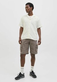 Lys gul kortærmet skjorte med en subtil tekstur, knaplukning foran, sammen med brune cargo shorts med sidelommer og sorte sneakers.