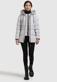 Lysegrå pufferjakke med hætte, quiltet design, lynlås foran og snoretræk detaljer. Parret med sorte leggings og kraftige sorte støvler.