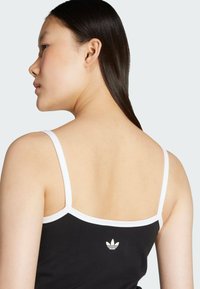 Černý top bez rukávů s bílými ramínky, na zadní straně s malým bílým logem. Hladká textura a přiléhavý střih.