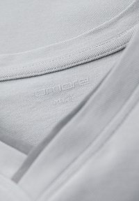 Gros plan d'un col en tissu gris clair montrant une texture fine et une étiquette de marque discrète embossée à l'intérieur du col.