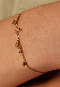 Gouden kettingarmband met kleine platte bedels en kralen, met een delicate textuur en minimalistisch ontwerp.