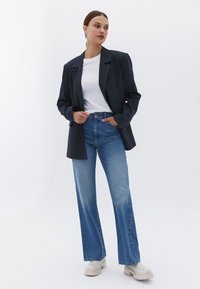 Tmavě šedý blazer, bílý tričko, světle modré džíny s vysokým pasem a béžové robustní boty. Hladká textura, přizpůsobený design, uvolněný střih.
