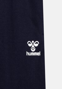 Tummansininen kangas, jossa on valkoinen logo, jossa on tyylitelty mehiläissuunnittelu ja sana "hummel" alla. Tasainen pinta, ei näkyviä kuvioita.
