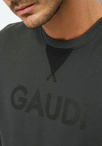 Felpa grigio scuro con lettering testurizzato "GAUDI", colletto a girocollo a costine e un dettaglio accentato triangolare nero a contrasto.