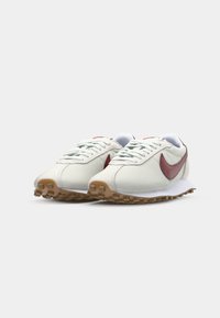 Športové tenisky s hornou časťou z ľahkej šedej sieťoviny, burgundským „swoosh“, bielymi akcentmi a štruktúrovanou gumenou podrážkou pre lepšiu trakciu.