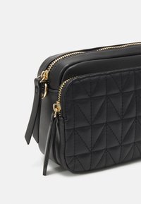 Pochette nera in pelle con doppia zip, caratterizzata da un motivo trapuntato con forme geometriche, accessori in metallo dorato e finiture laterali testurizzate.