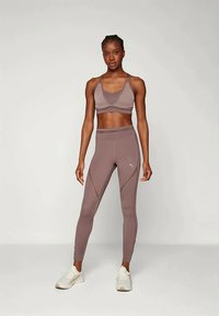 Sportos öltözet, amely egy mályva színű melltartót és hozzá illő, magas derekú leggings-t tartalmaz texturált részletekkel, fehér sportcipőkkel párosítva.