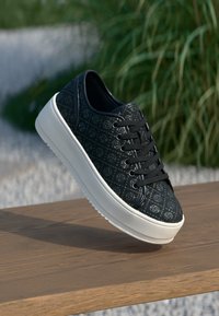 Sneaker nera con una toma a motivi, lacci rotondi e una spessa suola in gomma bianca. Materiale testurizzato con un sottile lucido e dettagli di branding.