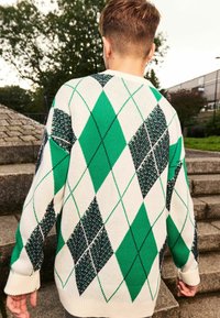 Zeleni i bijeli argyle pulover s oversized krojem, s dijamantnim uzorcima u tamnozelenoj i crnoj, pletenom teksturom i rebrastim manžetama.