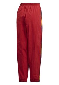 Červené polyesterové sportovní kalhoty s elastickým pasem, zakončené na kotnících a s vícebarevnými pruhy po stranách. Texturovaná, lehká tkanina.