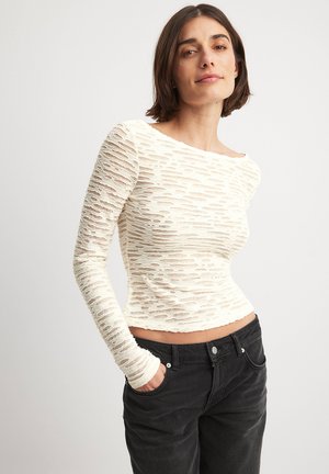 Ecrufarbener Langarm-Top mit einem strukturierten, ausgefransten Design. Verfügt über einen Boot-Ausschnitt und einen figurbetonten Schnitt, kombiniert mit hochgeschnittenen schwarzen Jeans.