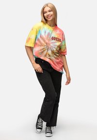 Mångfärgad tie-dye oversized t-shirt med snurrande pastellnyanser, korta ärmar och "49ERS" tryckt i rött. Bärs med svarta jeans.