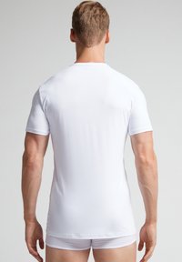 Biała koszulka z krótkim rękawem wykonana z gładkiego materiału, z klasycznym okrągłym dekoltem i dopasowanym krojem, widok z tyłu pokazujący minimalne szwy.