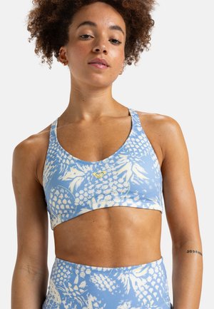 Sports bra in light blue with a floral print in yellow, featuring a wide band and adjustable straps for support and comfort.