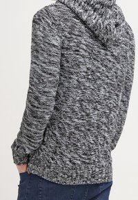 Kapuzensweatshirt in Schwarz-Weiß-Strick mit strukturiertem Muster, geripptem Saum und Bündchen. Es hat eine lockere Passform und mittlere Dicke.