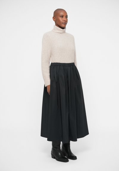 Beige strikket turtleneck top parret med en sort, plisseret, ankellang nederdel. Sorte, mellemhøje læderstøvler fuldender outfittet.