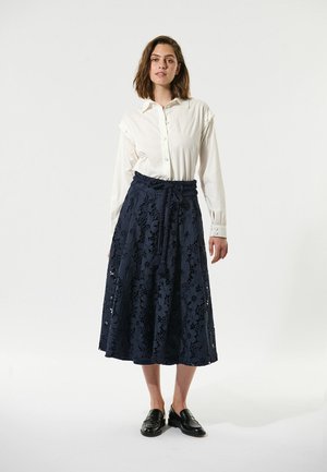 Witte langsemige shirt met knopen aan de voorkant, gecombineerd met een marineblauwe midi rok van kant met bloemenpatronen, een taille met trekkoord en een gelaagd ontwerp.