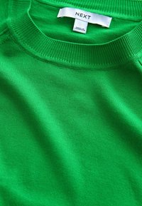 Pull vert en tissu doux avec un col et un ourlet côtelés. L'étiquette indique la marque "NEXT" et les détails de fabrication.