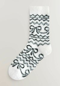 Bolondos fehér zokni fekete örvénymintákkal és masnikkal, puha textúrával és kerek orrformával.