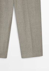 Pantalon gris clair en tissu texturé, avec une coupe droite et un motif chevrons subtil. Aucun élément métallique visible.