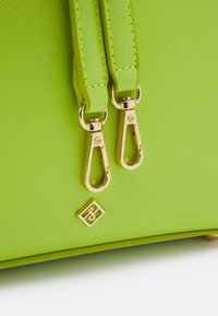 Groene gestructureerde handtas met gouden hardware; voorzien van dubbele handvatten en een metalen logo-accent. Glad oppervlak met een heldere kleurafwerking.