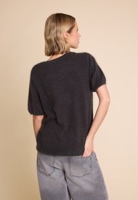 Mørk grå, myk strikkegenser med korte ermer og løs passform. Avsluttet med rund hals og subtil tekstur. Båret med lysegrå bukser.