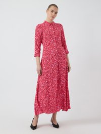 Robe chemise rouge à fleurs avec des manches trois-quarts, jupe fluide et chaussures pointues noires. Le tissu présente de petites fleurs roses et blanches.