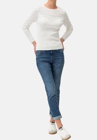 Maglione bianco a coste a maniche lunghe con una yoke a motivo pizzo; abbinato a jeans in denim arrotolati e sneakers bianche con suole beige.