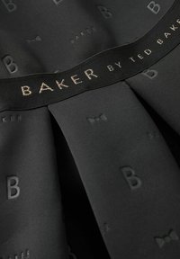 Juodas pūstas suknelė su lygia tekstūra, iškilusiu 'B' raštu ir juodu diržu, ant kurio metaliniu siūlu išvesta "BAKER by TED BAKER".