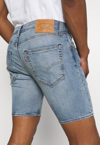 Vaalean siniset farkkushortsit, joissa on haalistunut pinta. Niissä on kaksi takataskua, erivärinen tikkaus ja vaaleanruskea nahkainen merkkilapuke vyötäröllä.