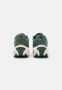 Sötétzöld sneaker cipők texturált dizájnnal, kiemelkedő fehér sarokkal, logó díszítéssel és vastag, párnázott talppal.