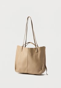 Μπεζ δερμάτινη τσάντα ώμου με δύο μακριά λουριά, υφή στην επιφάνεια και ευρύχωρο ανοιχτό άνω μέρος. Δεν διαθέτει ορατά μεταλλικά μέρη ή διακοσμήσεις.