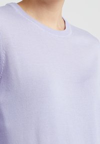 Pull à col rond violet clair en maille douce. Présente un col côtelé et une texture lisse avec des détails de coutures subtils.