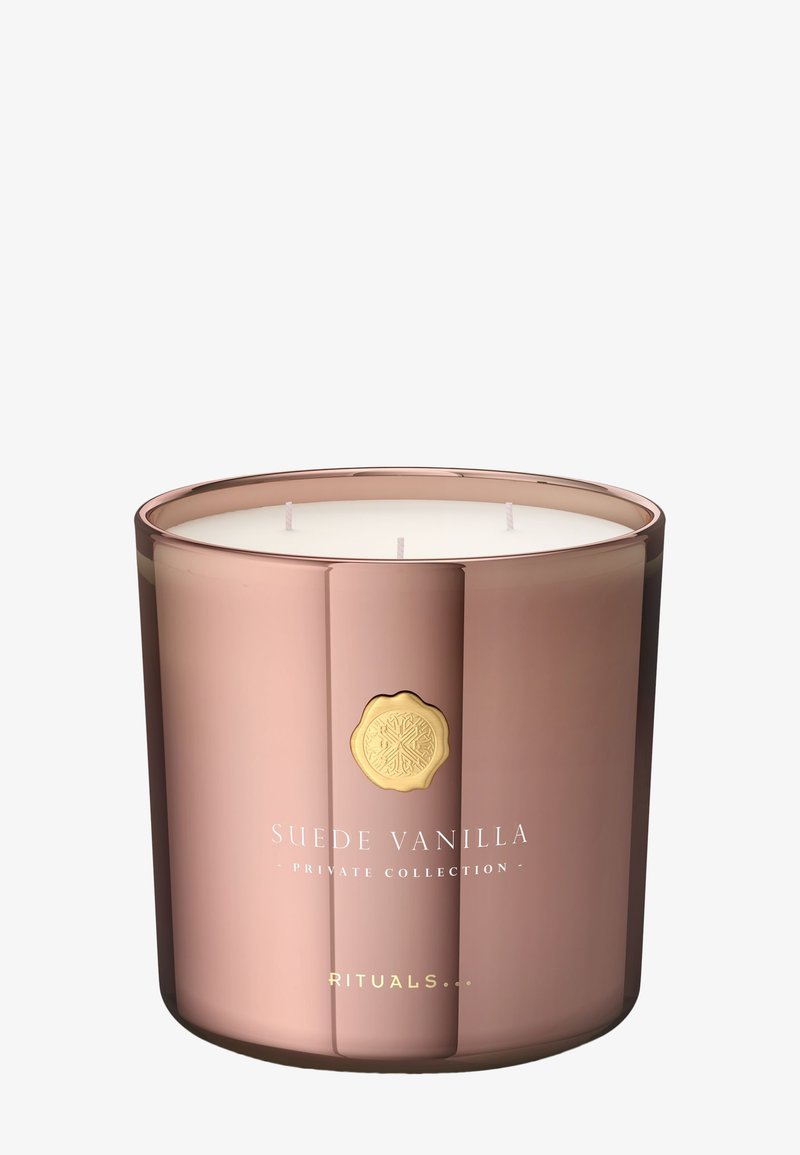 Portavelas de oro rosa con tres mechas, cera blanca y un emblema dorado. El texto dice "Suede Vanilla Private Collection Rituals."