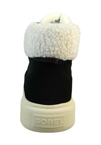 Svart semsket boot med en hvit, fluffy krage, med en kremfarget gummisåle. Baksiden har det pregete "SOREL" logoen.
