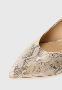 Kengät, joissa on terävä kärki ja metallinhohtoinen käärmeennahkakuosi, beige pohja tummanharmailla kuvioilla ja tyylikäs, sileä pinta.