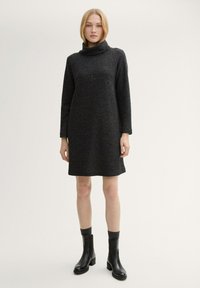 Schwarzes Rollkragenkleid mit langen Ärmeln, strukturierter Stoff, knielanger Schnitt, getragen mit schwarzen Stiefeln und grauen Socken.