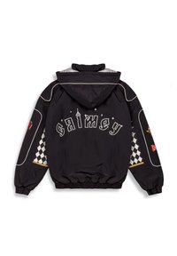 Chaqueta negra con capucha y puños elásticos, con el texto blanco "GRIMEY" y detalles de patrón en tablero de ajedrez en las mangas. Tejido texturizado.