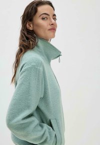 Mintgrüner Reißverschluss-Fleecejacke mit hohem Kragen, strukturiertem Stoff, seitlichen Taschen und minimalistischem Design, das eine lockere Passform bietet.