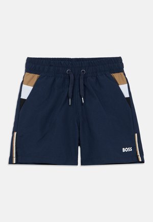Marineblå badshorts med elastisk midjebånd, kontrastfargede sidepaneler i brunt, hvitt og svart, og en logo på forsiden.