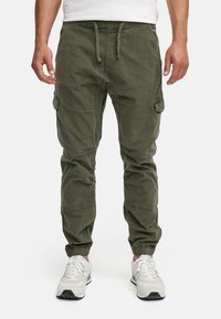 Pantaloni cargo verde oliva con vestibilità affusolata, polsini elastici, vita regolabile e numerose tasche laterali. Materiale in misto cotone con finitura texturizzata.