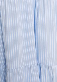 Vaaleansininen kangas, jossa on valkoisia pystysuoria raitoja, ja se on kerroksellinen muotoilultaan sekä pehmeätekstuurinen. Materiaali vaikuttaa kevyeltä ja hengittävältä.