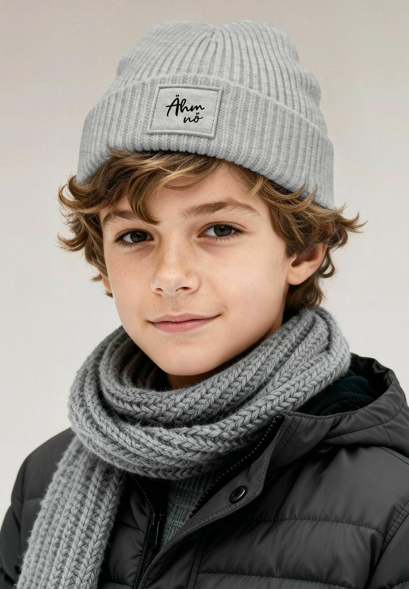 Gray ribbed beanie with a rectangular patch, paired with a thick, braided gray scarf, worn over a black puffer jacket. Subtle texture details visible.