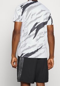 Camisa atlética de manga corta en blanco con patrones abstractos en negro y acentos texturizados, combinada con pantalones cortos negros que presentan un diseño de panel lateral.