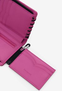 Różowy skórzany portfel z zamkiem błyskawicznym, wytłaczanym wzorem i miejscem na karty. Posiada czarne szwy i logo 'Desigual'.