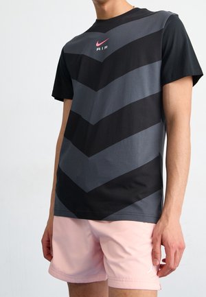 Nike T-shirt featuring a horizontal chevron pattern in black and gray, with a pink logo, paired with pink shorts. Material is smooth cotton blend.