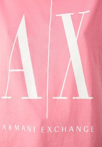 Różowa bawełniana koszulka z dużymi białymi literami "A" i "X" oraz napisem "ARMANI EXCHANGE" mniejszymi literami poniżej, gładka tekstura, casualowy design.