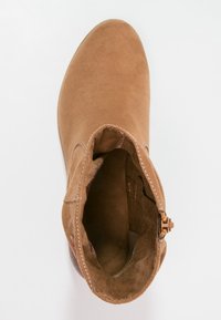 Braune Wildleder-Stiefelette mit runder Zehenform, sichtbaren Nähten und einem seitlichen Reißverschluss. Das Innere bietet eine weiche Fütterung; minimalistisches Design.