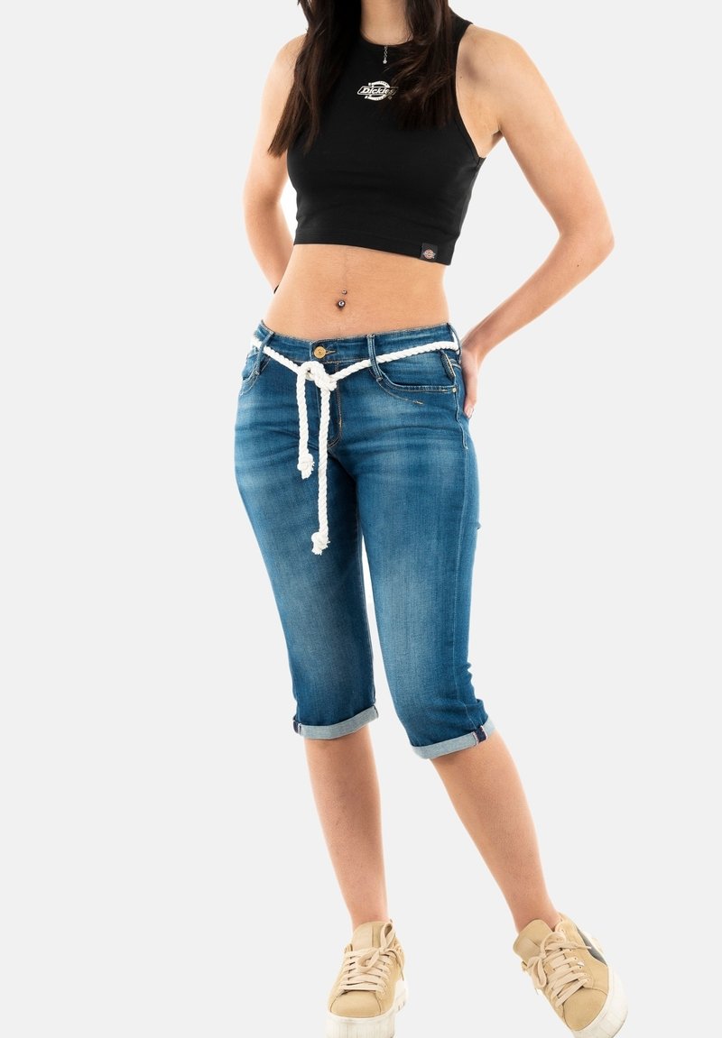 Jeans capri en denim bleu délavé avec des manches retroussées, cordon blanc et bouton métallique. Associés à un crop top sans manches noir.